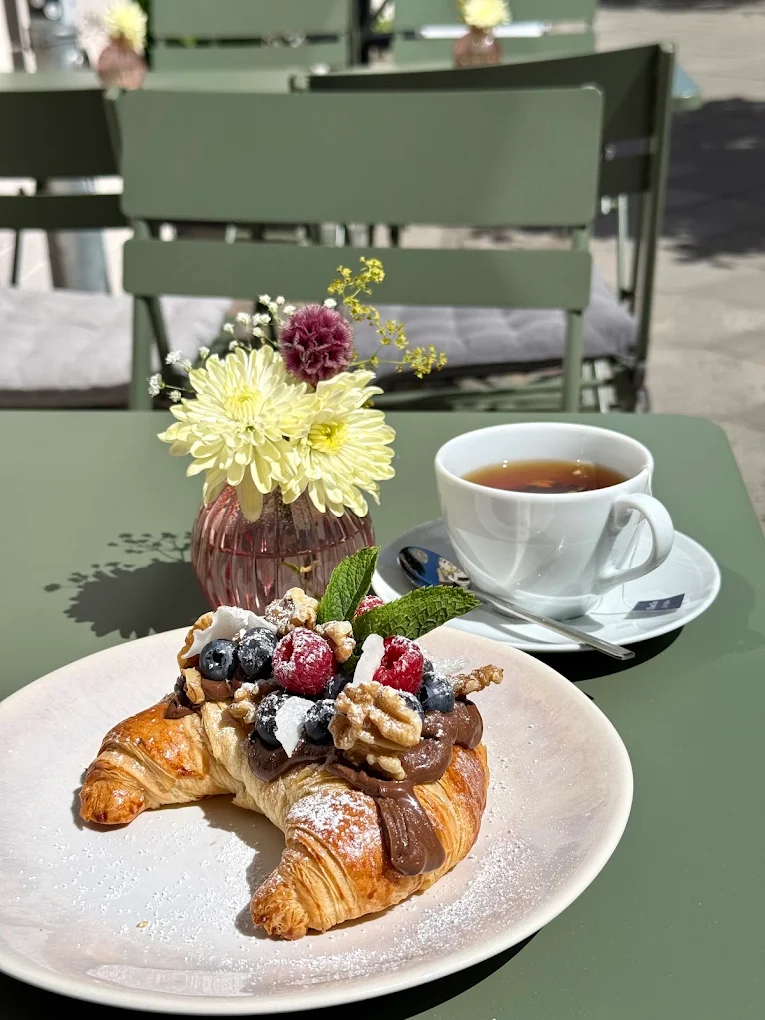 Croissant mit Schokocreme, Beeren und Walnüssen, dazu Tee, an einem Tisch draußen