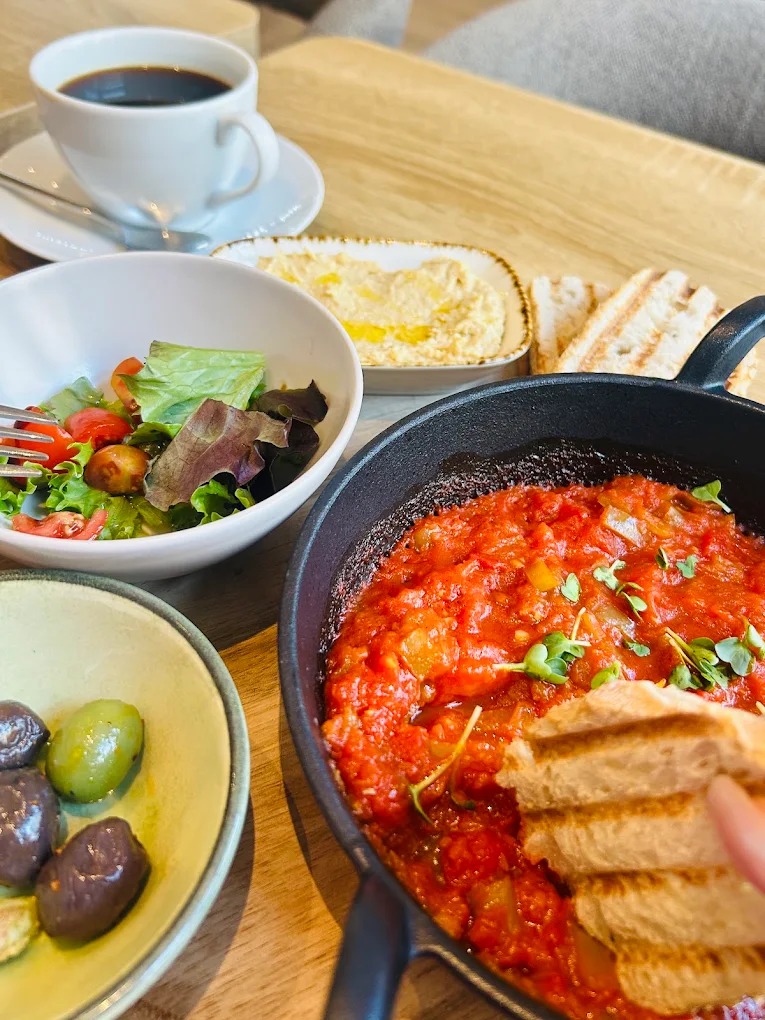 Frühstück mit Tomatenpfanne, Hummus, Salat, Oliven, Brot und Kaffee