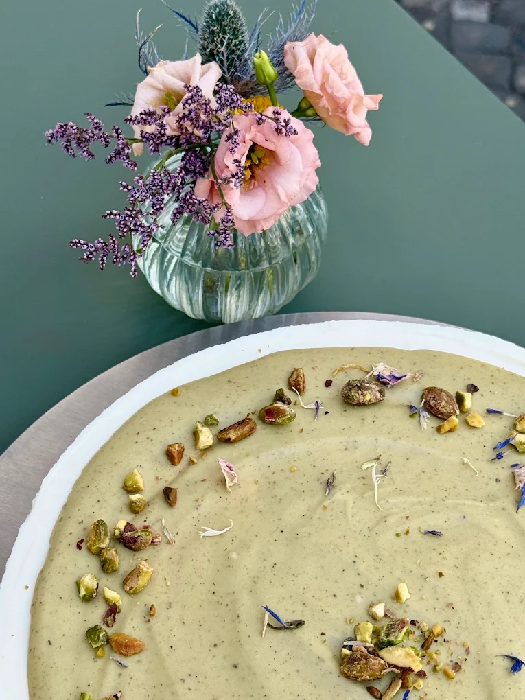 Pistazienkuchen mit gehackten Pistazien und Blüten, daneben ein Blumensträußchen